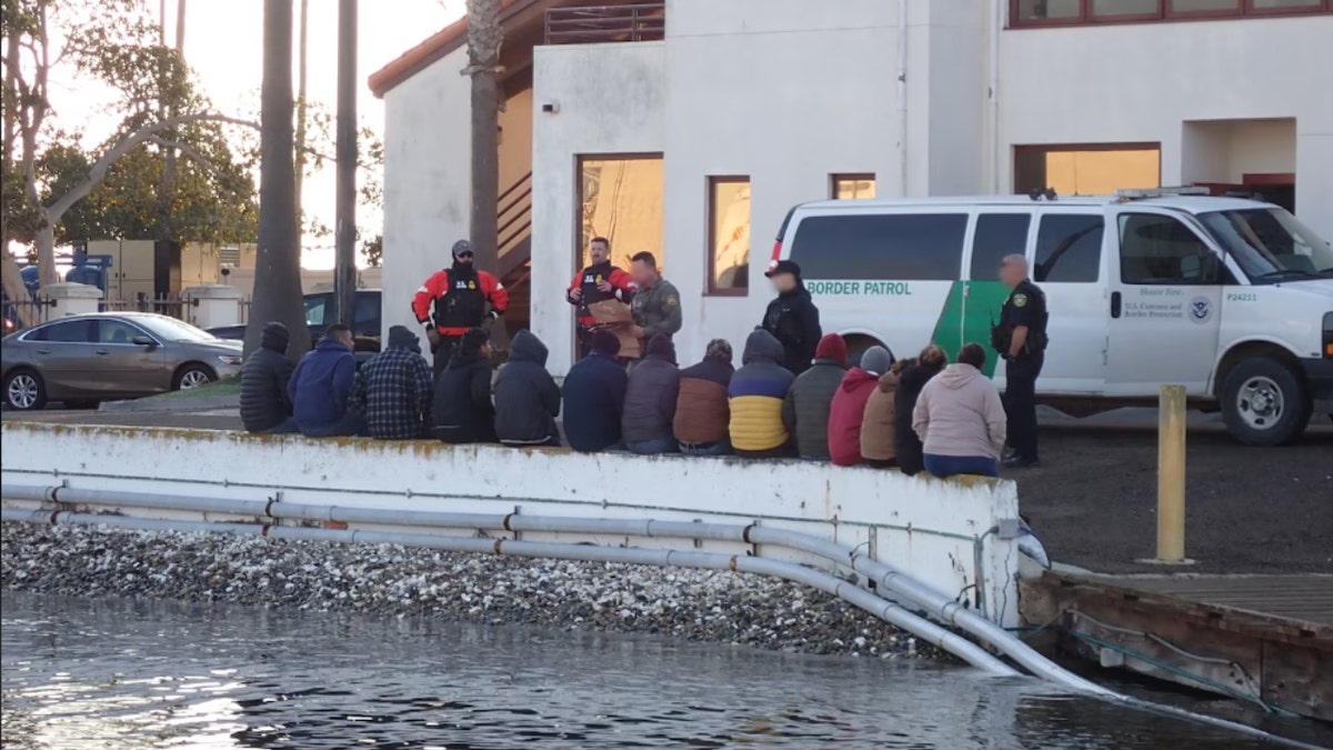 The boat passengers sitting outside a Border Patrol van