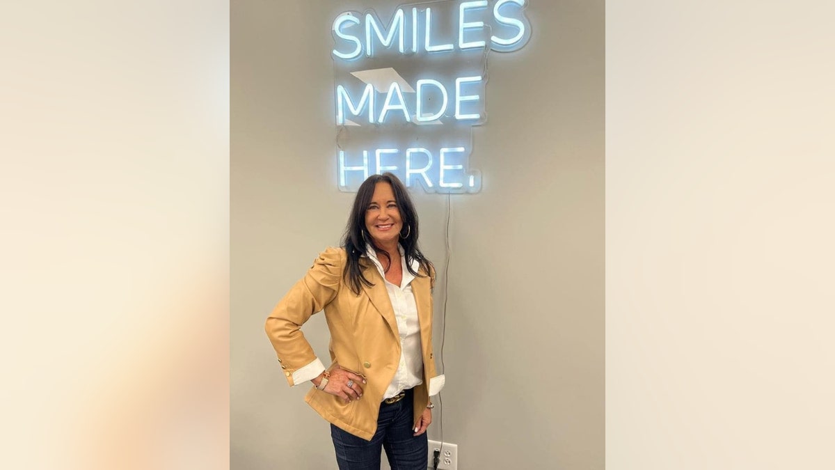 Suzanne Mericle poses beneath a neon sign that reads, "Smiles made here."