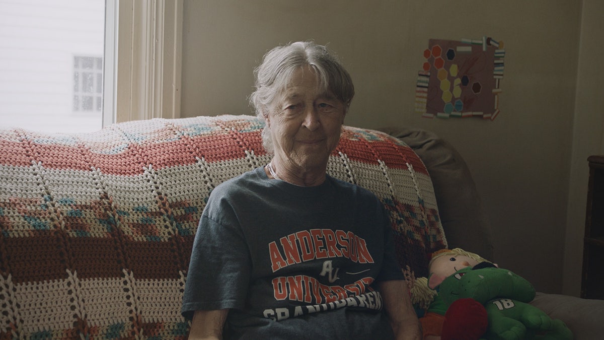 Sharon Livingston wearing a blue shirt with orange lettering sitting on a multi-hued couch.