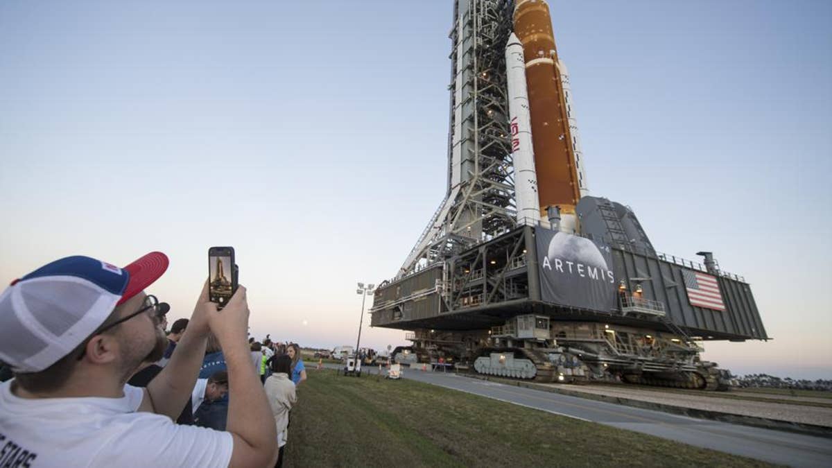 rocket on launchpad as man takes picture in foreground