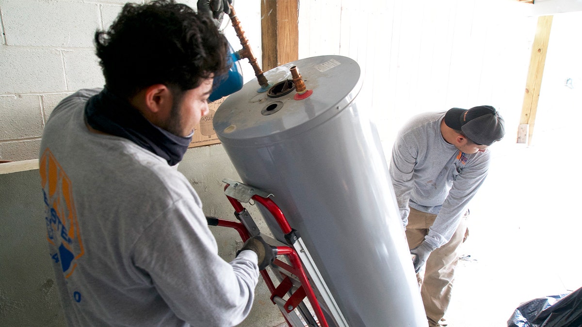 Angel Gomez, left, and Franes Mendez, technicians at heating, cooling and plumbing company John G. Webster, remove a gas water heater from a home in Washington, D.C., on Aug. 28, 2024.