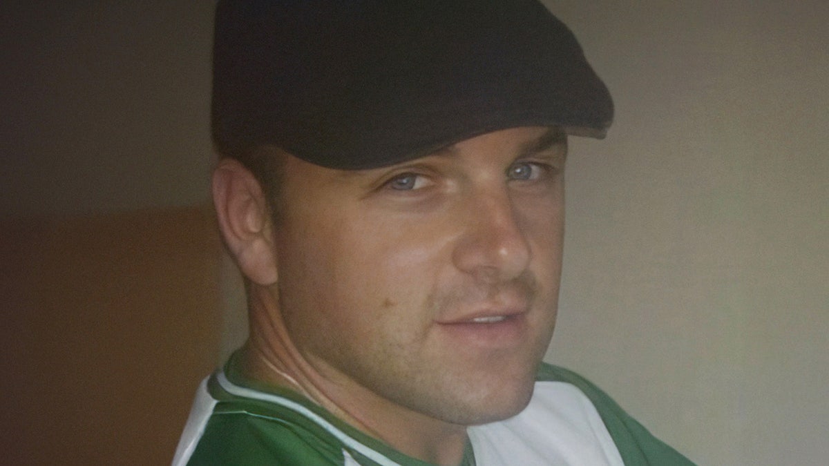 John O'Keefe wearing a green and white shirt and a black cap looking to the side.