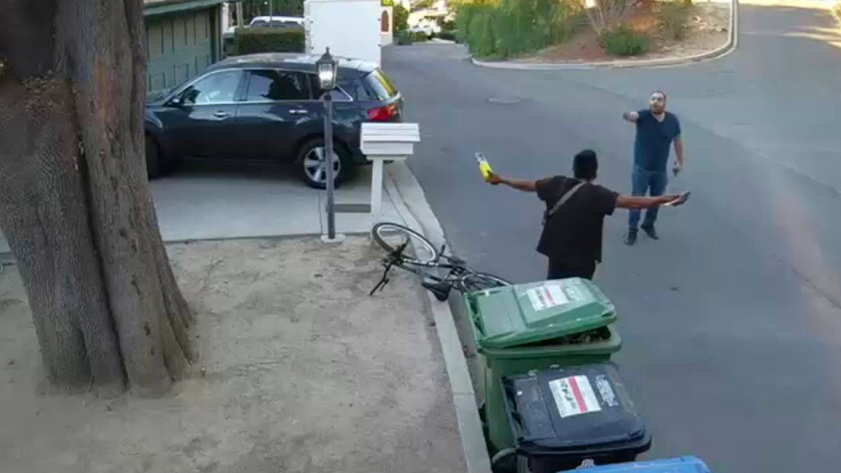 a man holding what appears to be a fuel tank and blowtorch nozzle as a homeowner confronts him