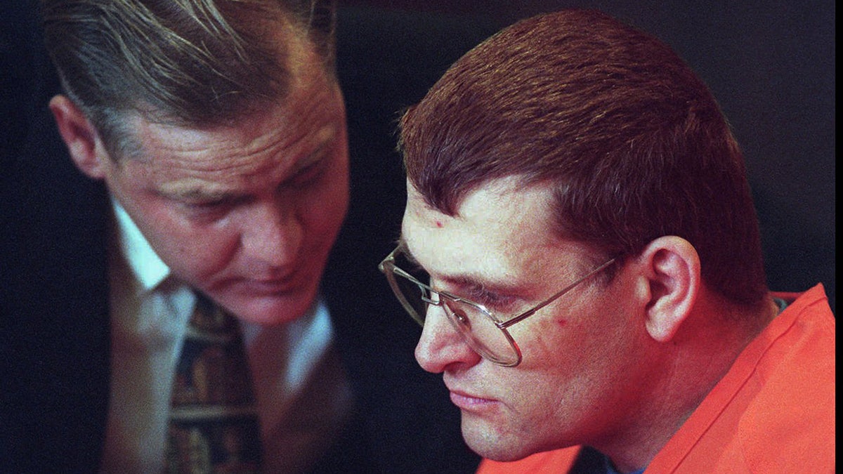 A close-up of Keith Jesperson in an orange jumpsuit listening to his attorney.