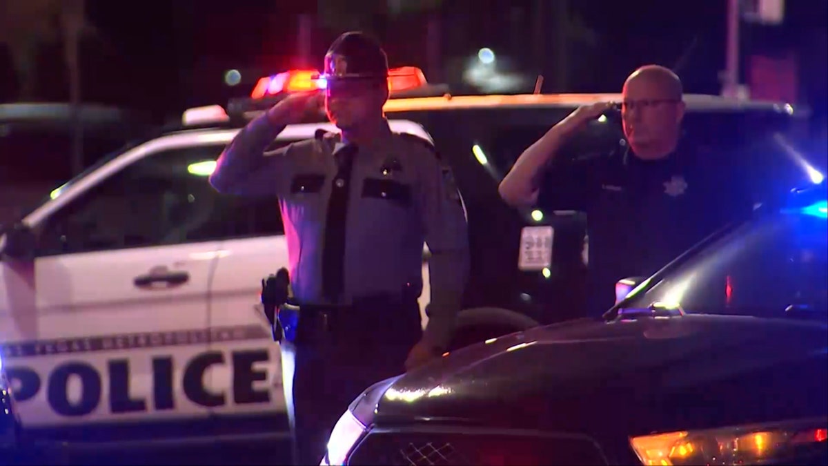 North Las Vegas Police Department (NLVPD) officers salute as other officers ride past on motorcycles in procession for a slain officer.