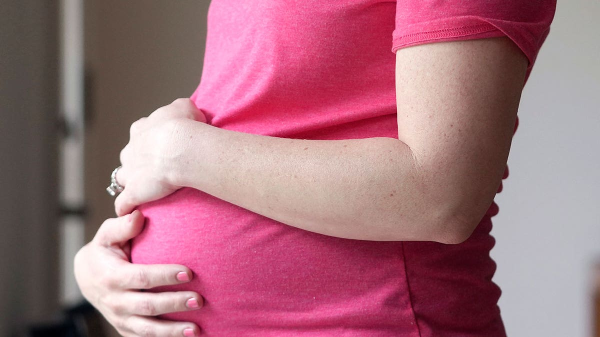 Pregnant woman in pink shirt holding her belly