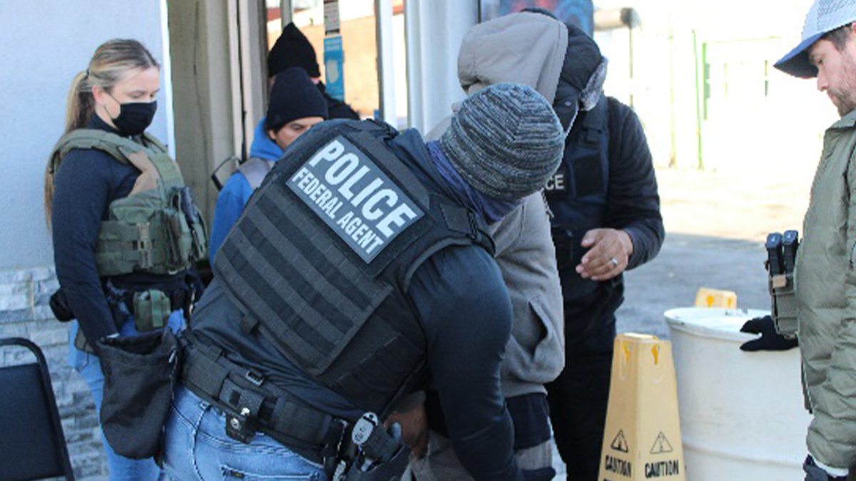 federal agent seen from back wearing vest arresting suspect