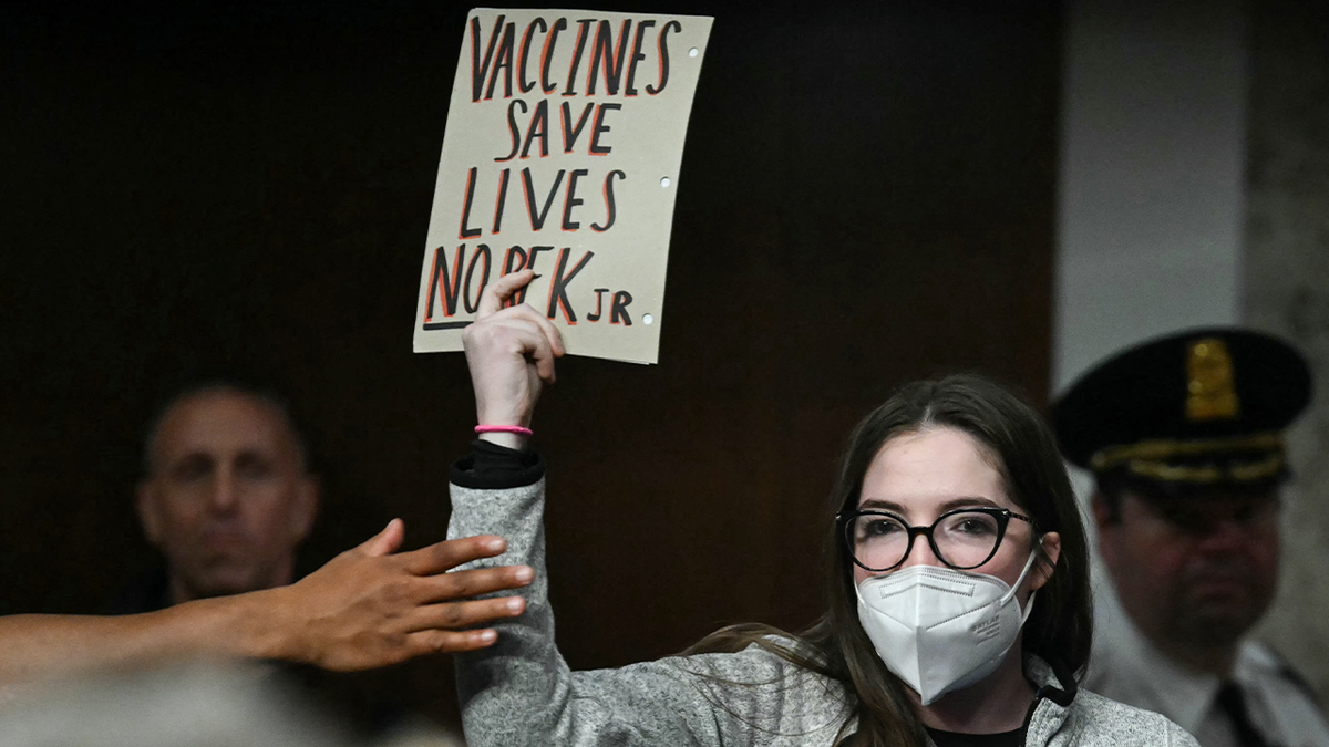 A protester holds up a sign reading "Vaccines save lives" as Robert F. Kennedy Jr. testifies during his Senate confirmation hearing on Capitol Hill, Jan. 29, 2025.