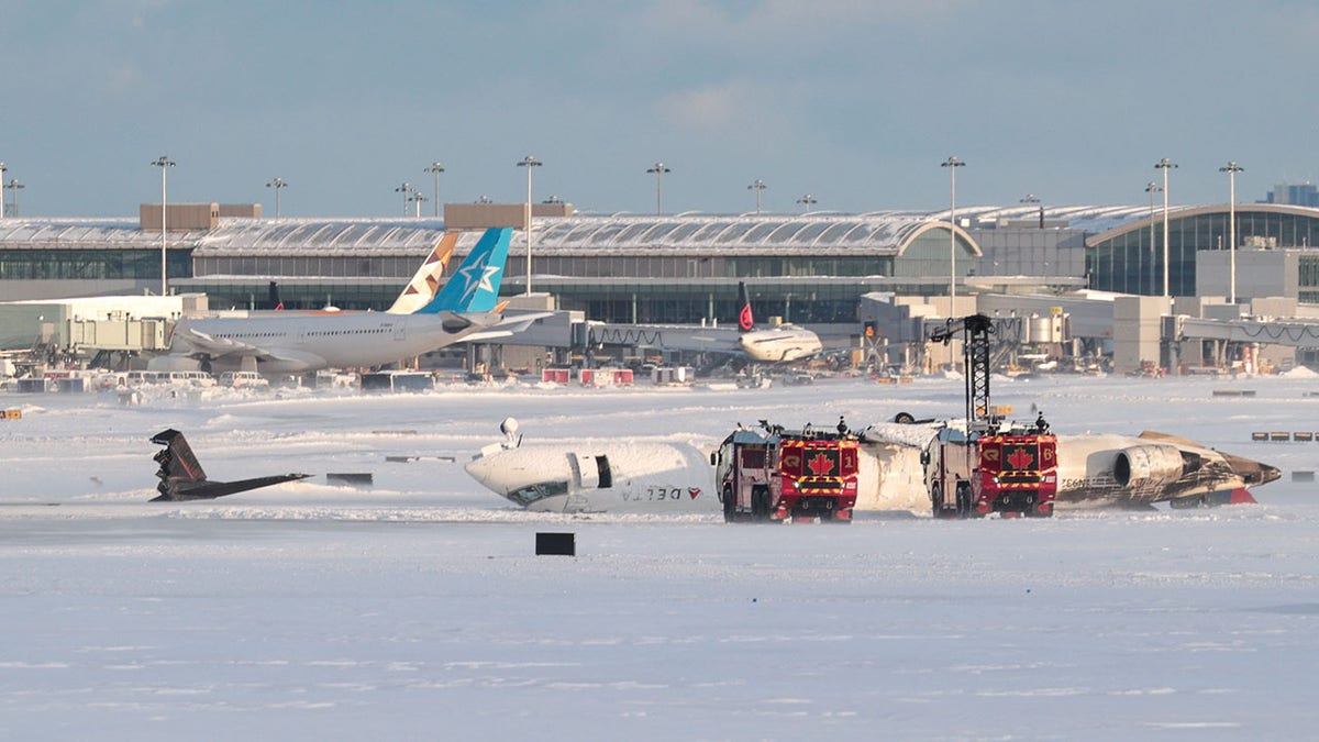 Emergency vehicles next to the flipped plane at a snowy Toronto airport tarmac