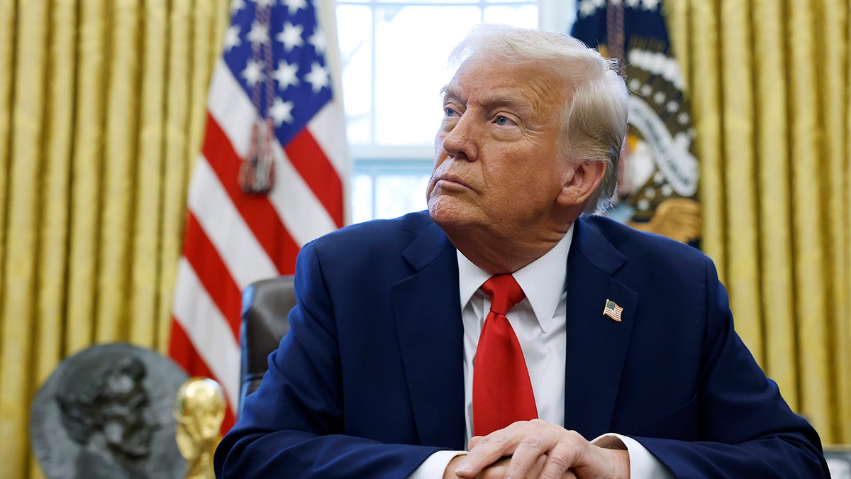 Donald Trump looking up wearing a blue blazer, a white shirt and a red tie sitting