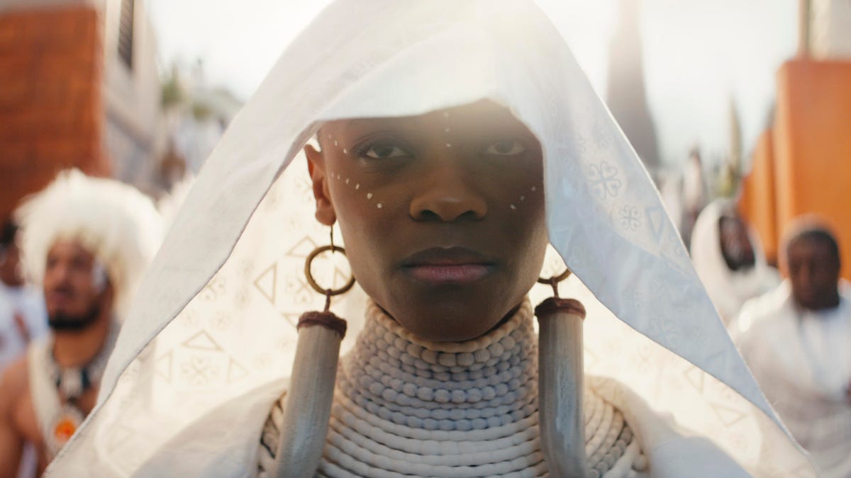 Letitia Wright as Shuri walks through a village in all white