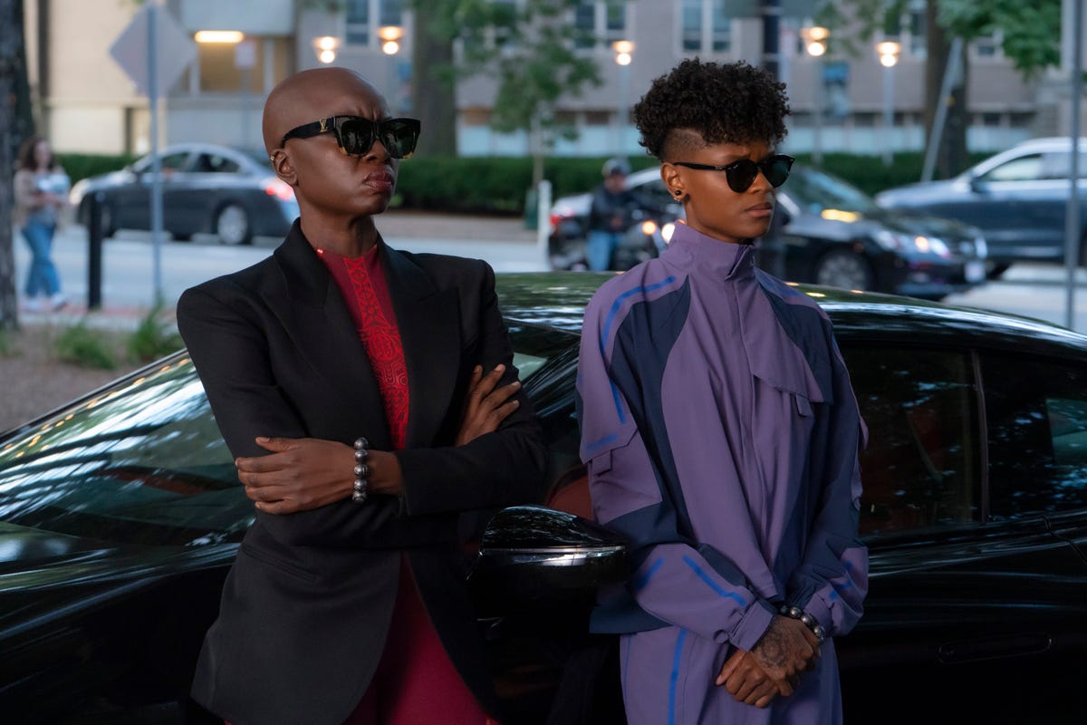 Wearing sunglasses, Okoye and Shuri stand by a car in Black Panther: Wakanda Forever