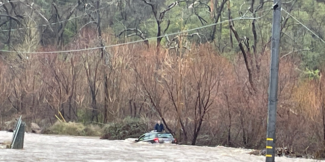 A man sits on the roof of his car after getting stuck in floodwaters.