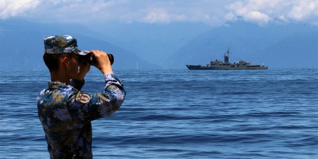 A People's Liberation Army member looks through binoculars during military exercises as Taiwan’s frigate Lan Yang is seen at the rear, on Friday, Aug. 5, 2022. China has repeatedly entered the waters and airspace of Taiwan in the past several weeks, Taiwan defense officials have said. 