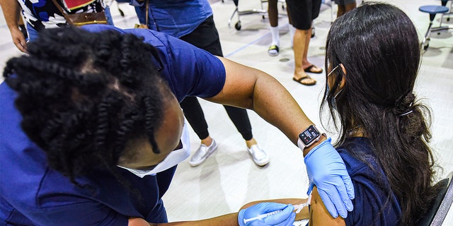 A nurse gives a girl a dose of the Pfizer vaccine at a COVID-19 vaccine clinic at Lyman High School in Longwood on the day before classes begin for the 2021-22 school year.