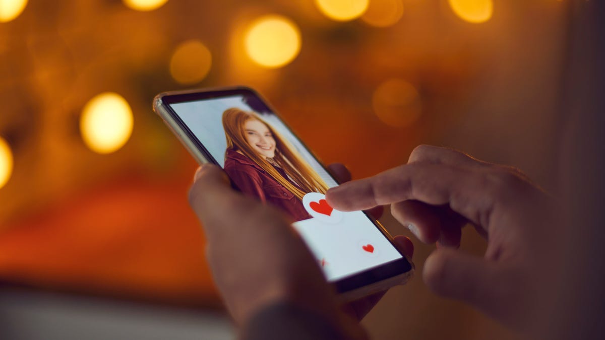 A pair of hands hold a phone with a dating profile on screen.