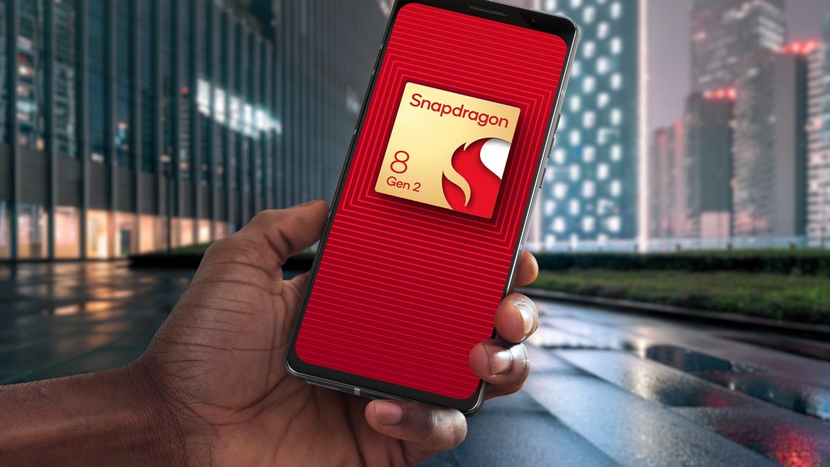 A phone with the Snapdragon 8 Gen 2 chip logo on its screen, held in front of a nighttime city landscape.