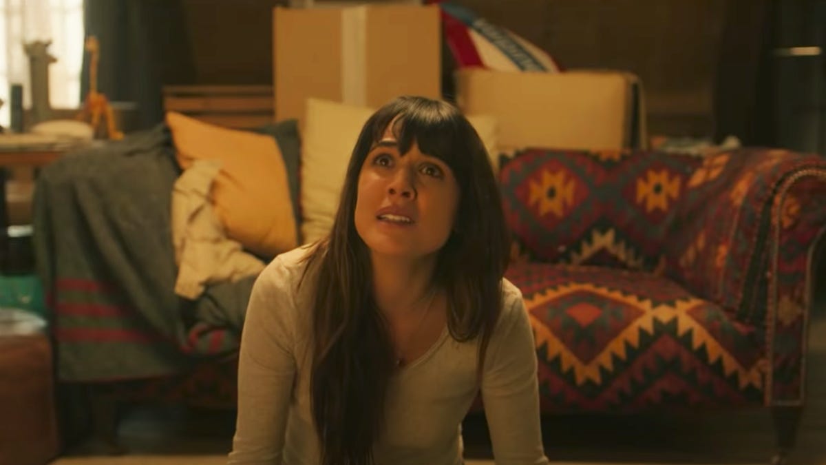 A woman sitting on the floor in a messy room looking worried