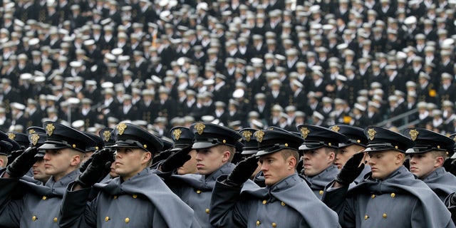 Army Cadets salute as they march on the field before an NCAA college football game against Navy.