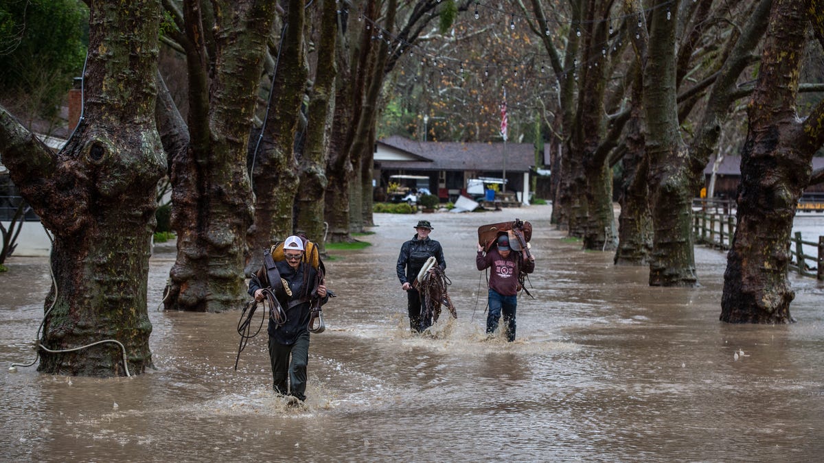 Three people walk knee-deep in floodwaters.