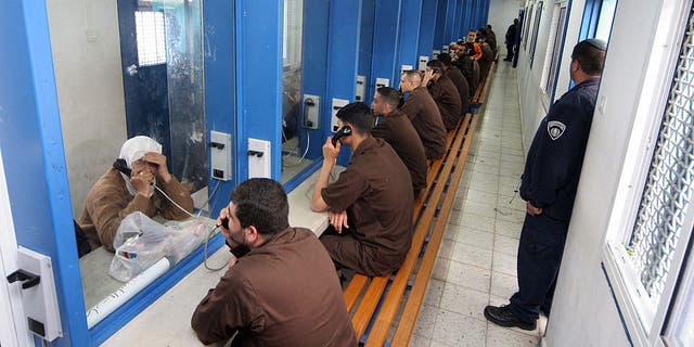 Palestinian men sitting in their brown prison uniforms behind glass talking on phones to relatives at the Gilboa Prison, east of the northern Israeli town of Afula. Most of the 850 adult male prisoners in this prison are serving very long jail terms and some are serving life sentences.