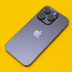 A deep purple iPhone 14 Pro with three cameras pointing upward lies on a yellow background