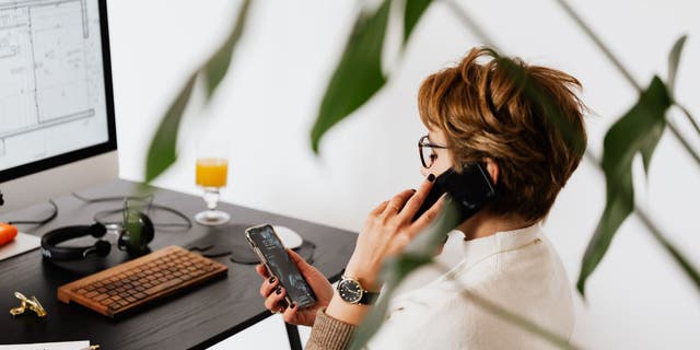 A woman talks on a phone while looking at a smartphone screen