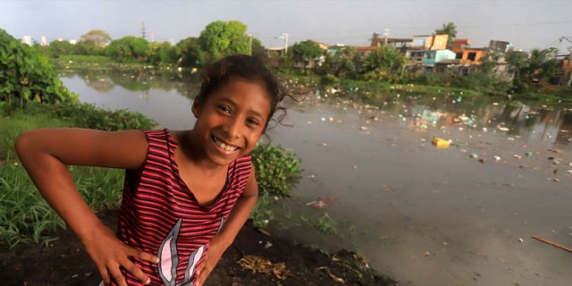 girl smiles near Brazilian river covered in litter