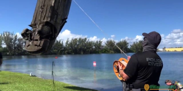 police officer looks on as submerged car removed from lake