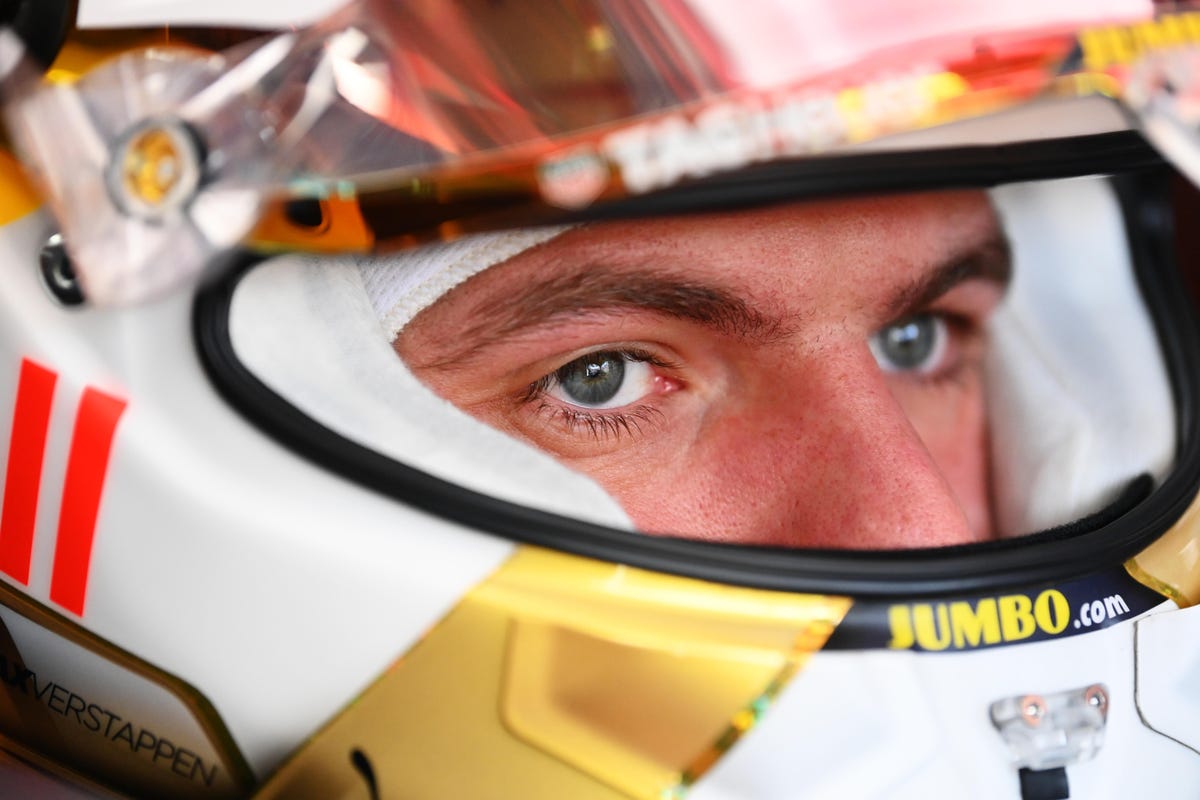 Max Verstappen appears focused as he stares out of his white and gold racing helmet.