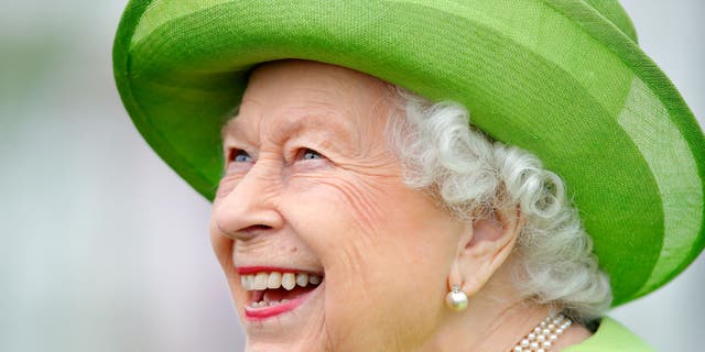 Queen Elizabeth gives a big smile while wearing a bright green coat with a matching hat.