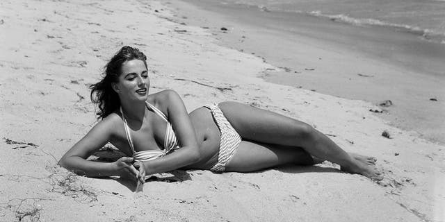 A glamour shot of Jackie Collins posing in a bikini at the beach