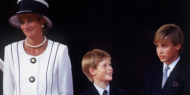 Princess Diana in a white and navy dress with a matching hat standing next to Prince Harry and Prince William