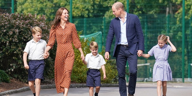 Prince William in a navy blazer and matching pants with a white shirt walking alongside his wife and their three children