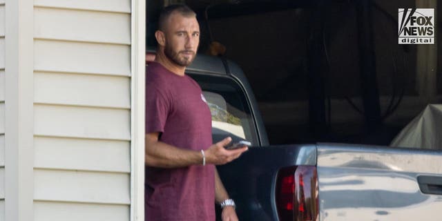 Richard Tobin in blue shorts and and a purple t-shirt looks suspicious as he peeks from the garage