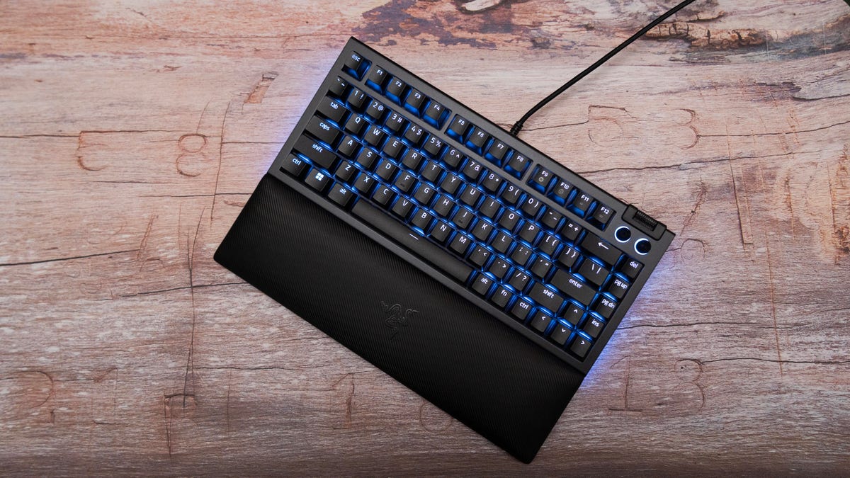 Razer BlackWidow V4 75% shown from above with its wrist rest and blue backlighting on a wood surface