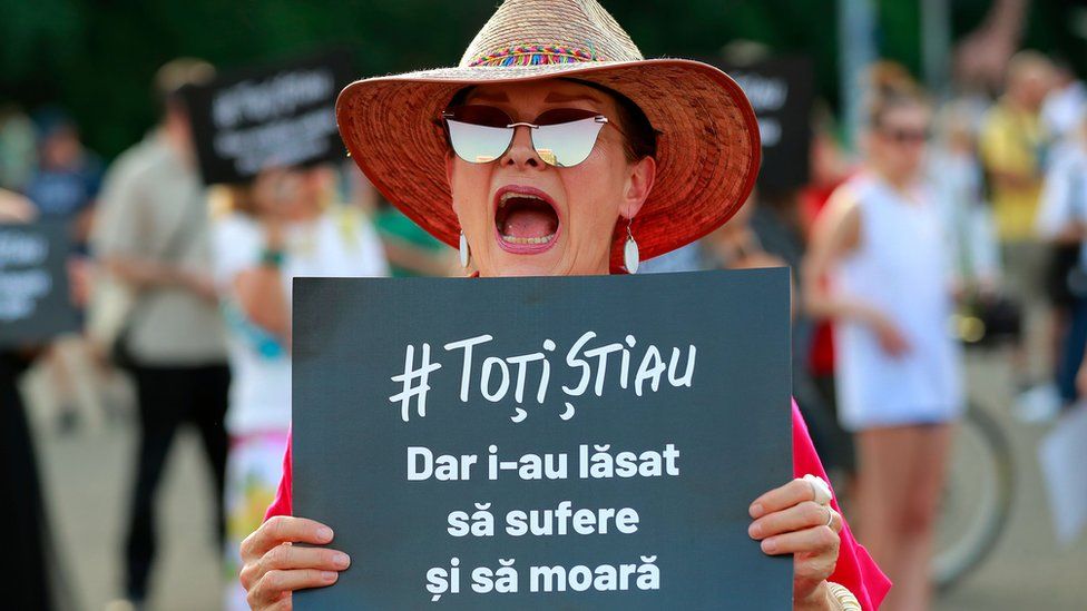 A woman protesting over elderly the elderly care scandal holds a placard which reads: "Everyone knew, but they let them suffer and die"