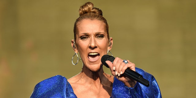 Celine Dion sings into a microphone with a high bun and electric blue dress with puffy shoulders