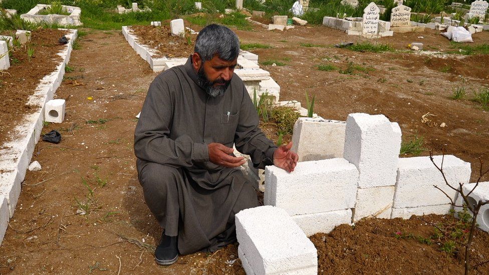 A man kneels next to a freshly-dug grave