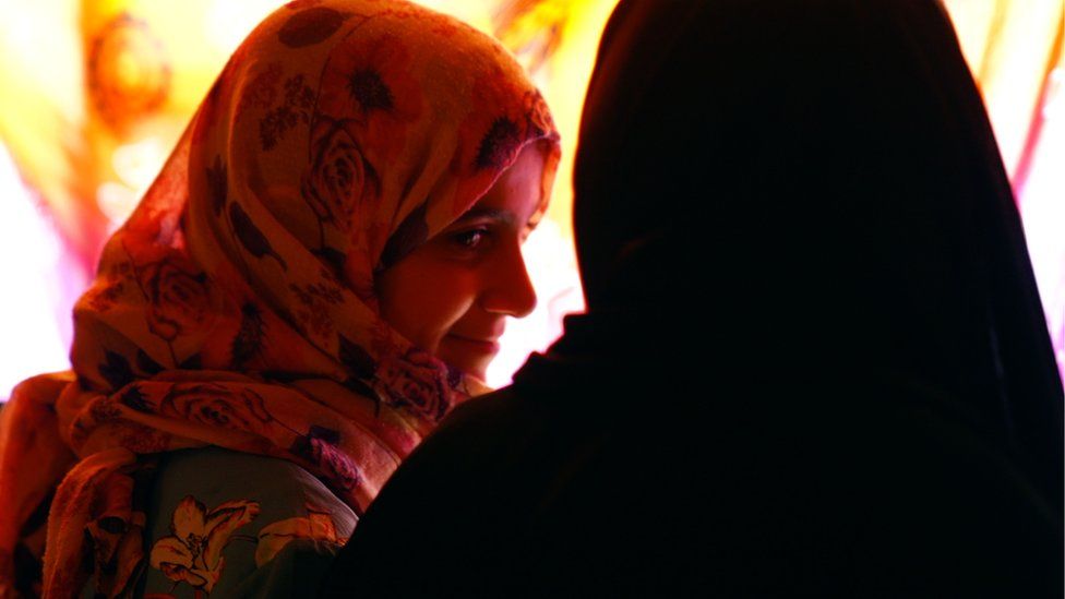 Two women with headscarves look at each other