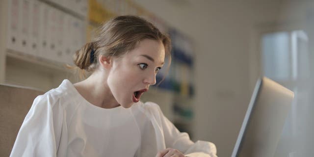 Woman looking at her laptop shocked at finding out that she has been scammed.