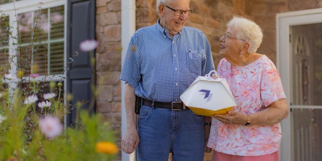 Elderly couple Paul and Susie Sensmeier outside their home, Susie is holding the Wing delivery order