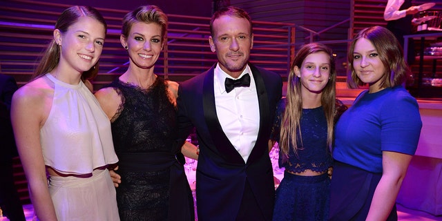 Maggie McGraw in a blush halter top and skirt smiles next to mother Faith Hill in a long black dress, husband Tim McGraw in a classic black tuxedo, daughter Audrey in a blue dress, and daughter Gracie in a blue dress