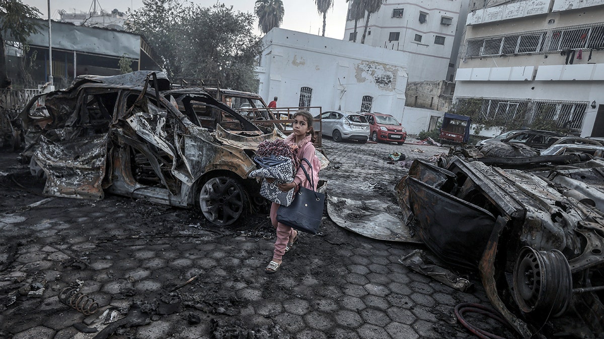 A girl tries to collect usable belongings amid wreckage of vehicles after Al-Ahli Baptist Hospital was hit in Gaza City, Gaza on October 18, 2023.