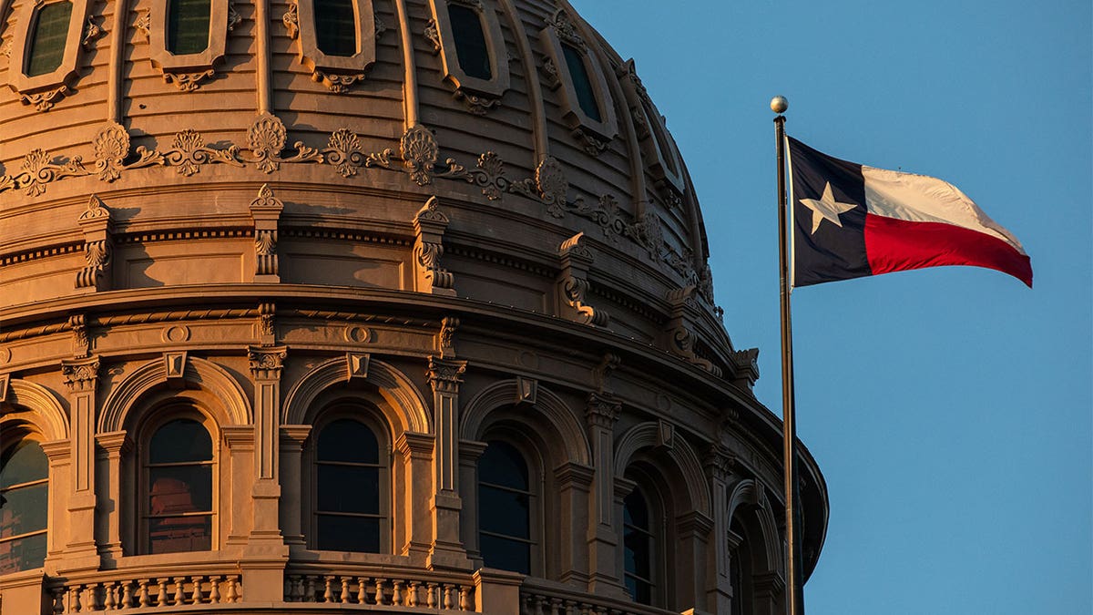 Texas Capitol building dome with the Texas flag waving in front.