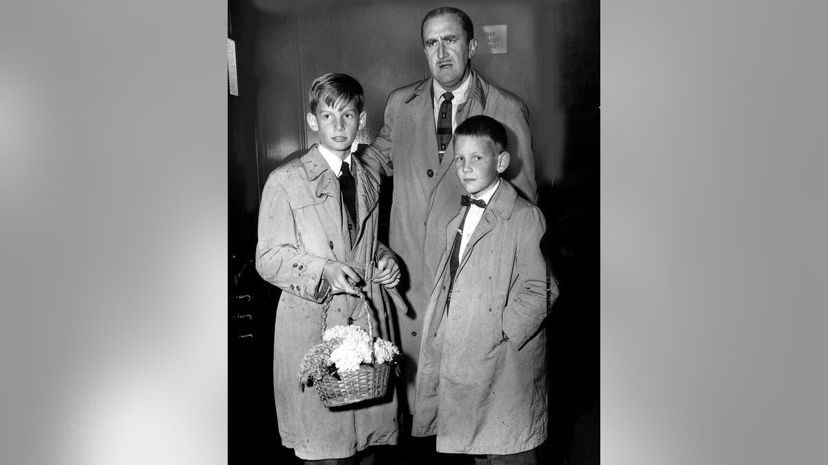 Annd Woodwards two sons looking somber with a male figure