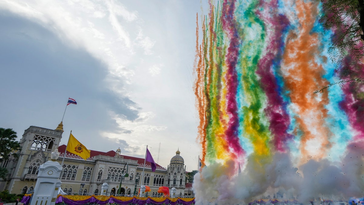 A rainbow of fireworks trails colorful smoke up into the sky outside of Thailand's government house, itself bedecked with orange and purple banners.