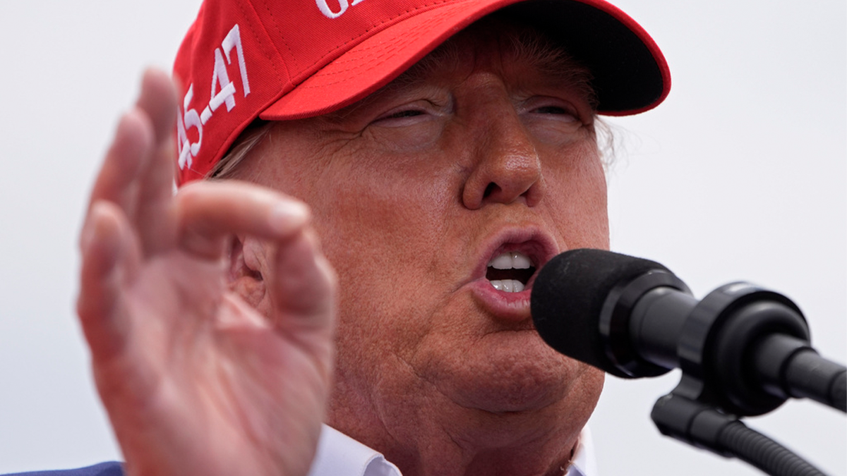 Trump speaking at a rally while wearing a red MAGA hat