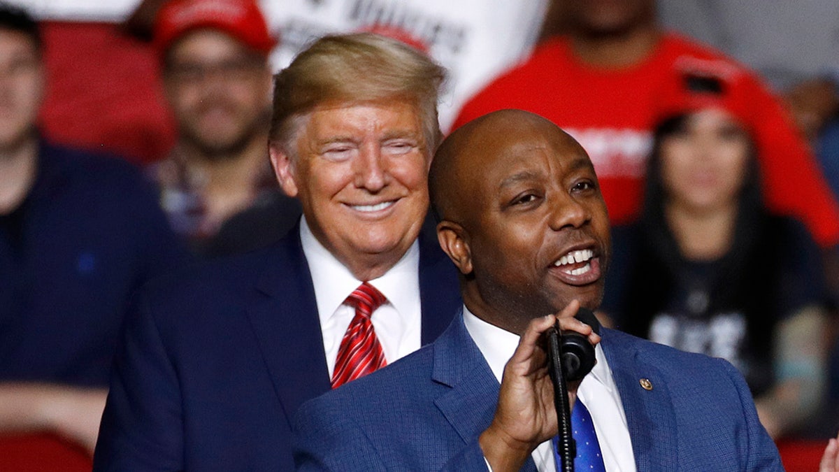 Tim Scott speaks on stage with Trump behind him