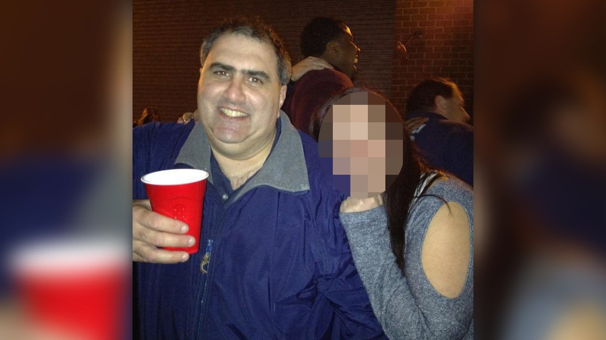 Joe Delucia holds a red cup as someone leans on his shoulder at a bar